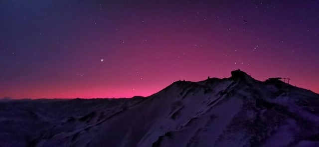 Red pre-dawn sky with stars and planets still visible over the top of snow clad mountain