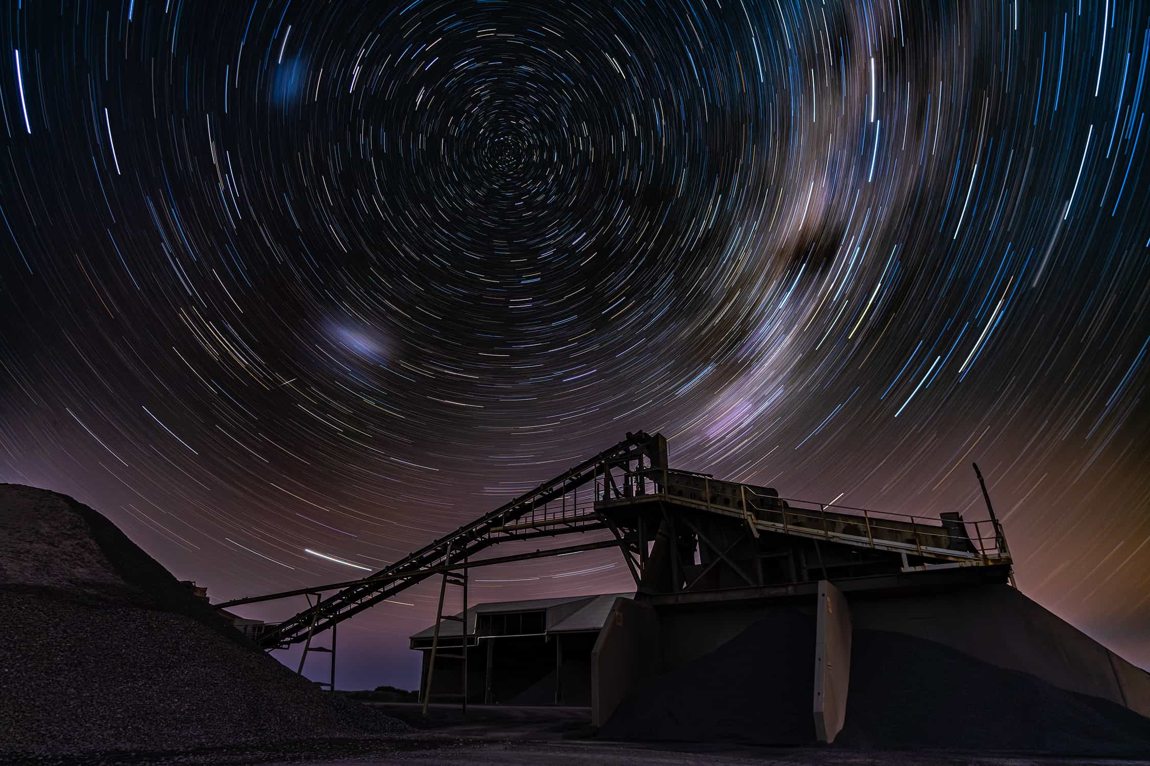 Very dark spooky image taken at Blackhead quarry in Dunedin. The artist set cammera setting to brightest daylight settings, with exception of exposure which had the camera fiming for over 1200 seconds. The image has brytal industrial quarry equipment and conveyor silhouetted against back drop of smooth circular star trails around South celestial pole.
