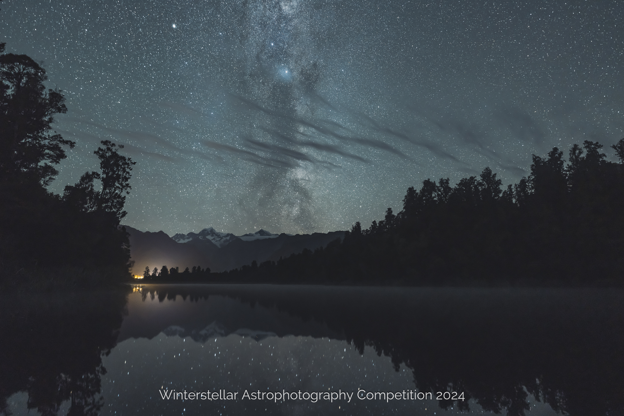 Milky way reflected in still waters of lake surrounded by forest.